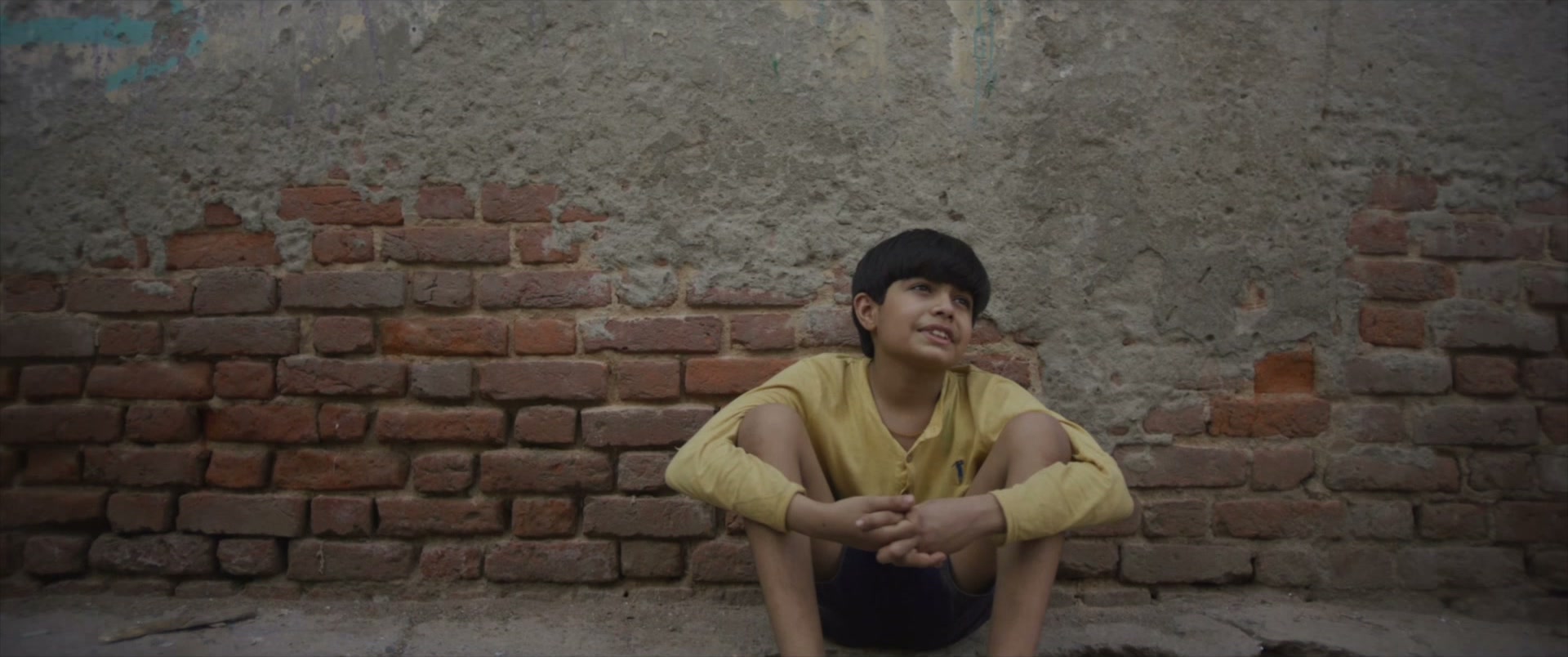 Boy sitting against a brick wall
